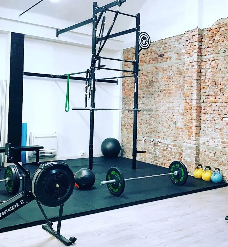 La sala di STC Milano in ordine: rack, bilanciere, kettlebell allineate e vogatore, davanti alla parete in mattoni a vista.